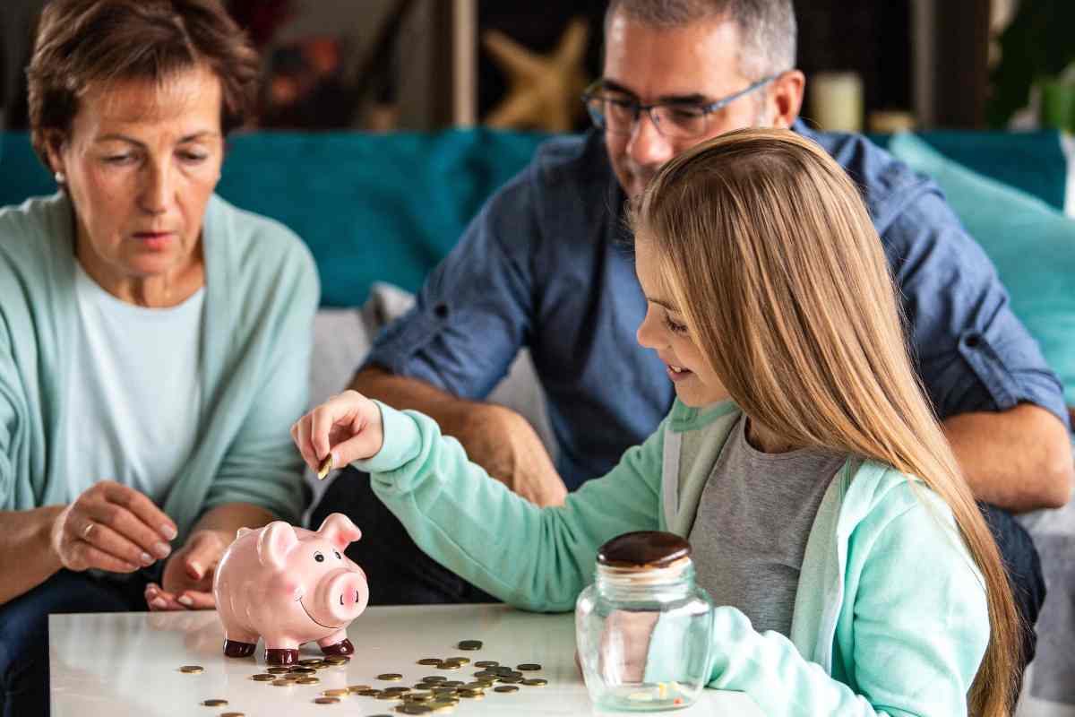 bambina mette in un salvadanaio delle monete vicino nonna e padre