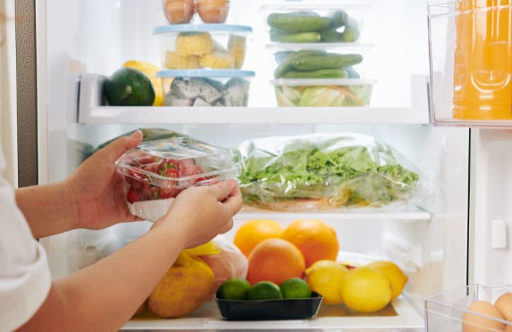 Pomodori in vaschetta tra le mani davanti a frigo aperto