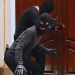 ladri incappucciati che tentano di aprire una porta con un piede di porco