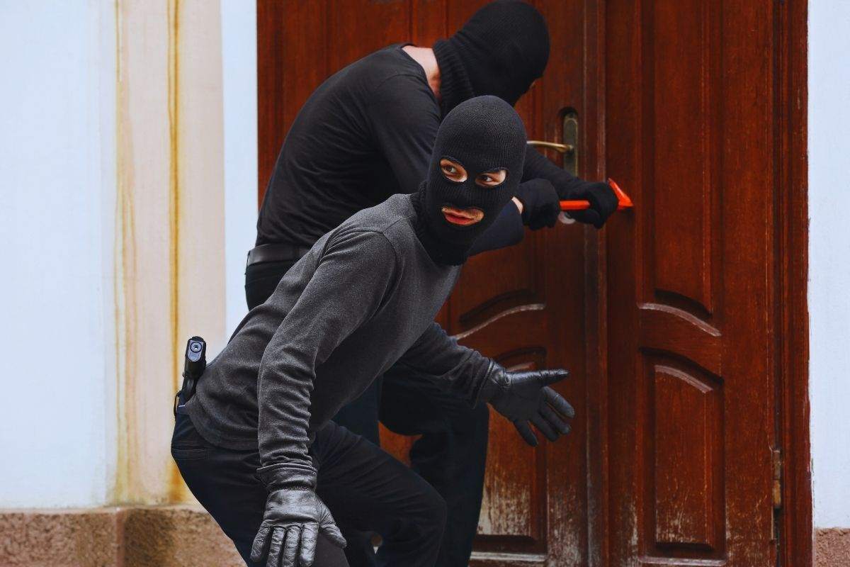 ladri incappucciati che tentano di aprire una porta con un piede di porco