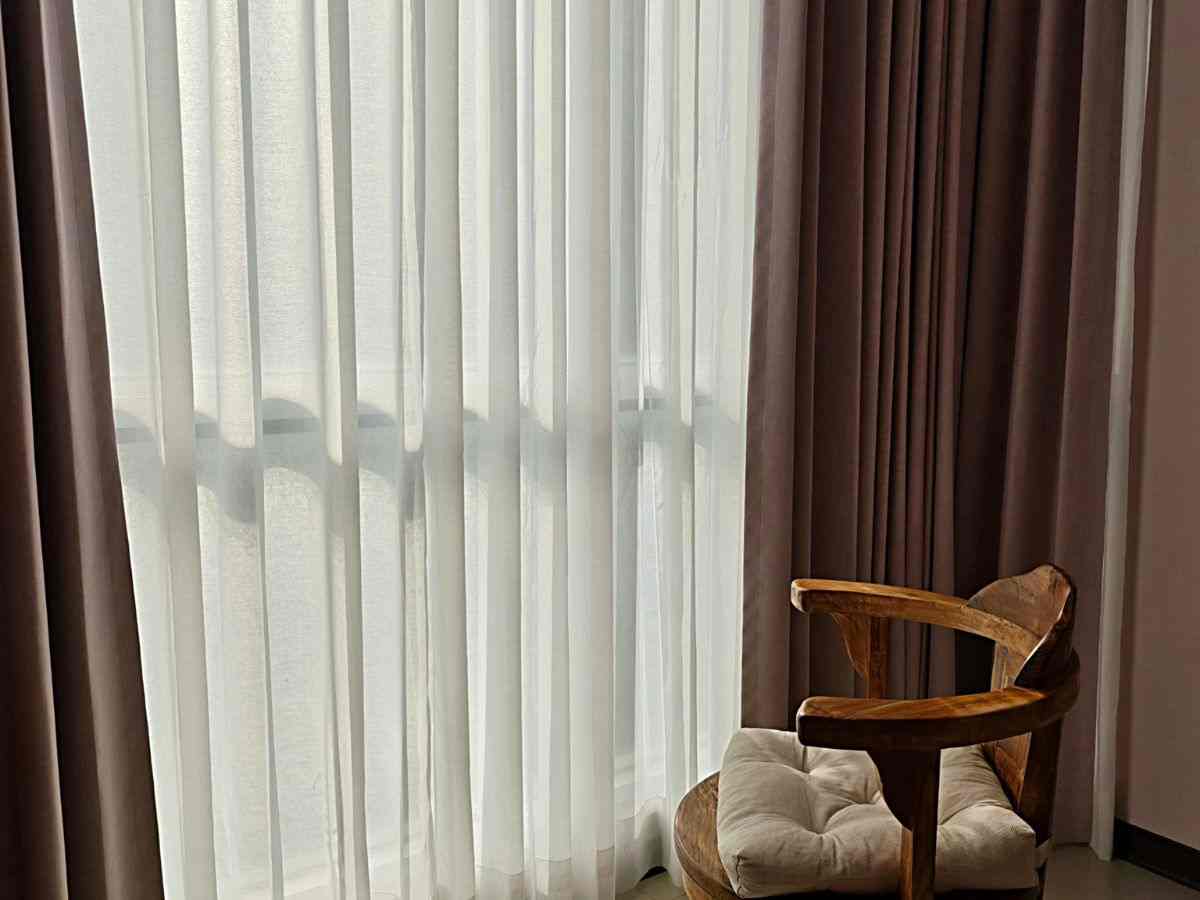 una poltrona vicino a una finestra coperta da tende bianche